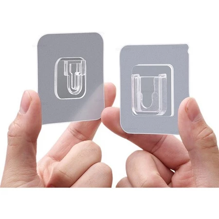 Quatro ganchos adesivos transparentes fixados em um azulejo de cozinha segurando utensílios domésticos e panos de prato